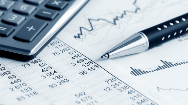 Image of finance numbers on a page with a pen and claculator visible
