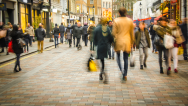 Image of a busy shopping highstreet with shapes of people walking on the street and shopping