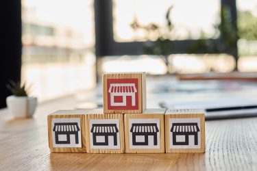 A wooden block with a miniature store on top, representing a creative franchise concept in a modern office setting.