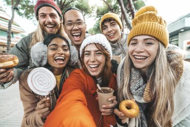 Happy friends wearing winter clothes taking selfie picture with smart mobile phone outside - Group of young people visiting Christmas market enjoying winter holiday together
