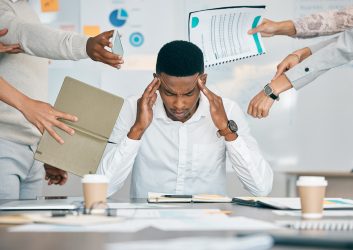 Stress, burnout and tired black man with headache, frustrated or overwhelmed by co-workers at workplace